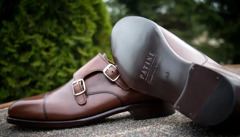 Eleganckie brązowe buty z podwójnymi klamrami, wykonane z wysokiej jakości kruponu. Widoczna podeszwa z logo marki.