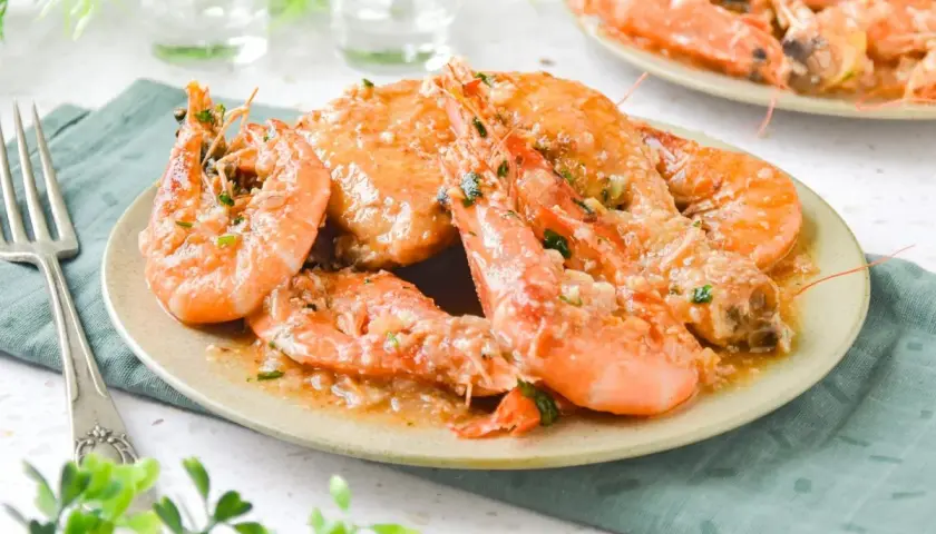 Plato de pollo con gambas en salsa de ajo y perejil, servido en un plato beige con un tenedor a la izquierda.