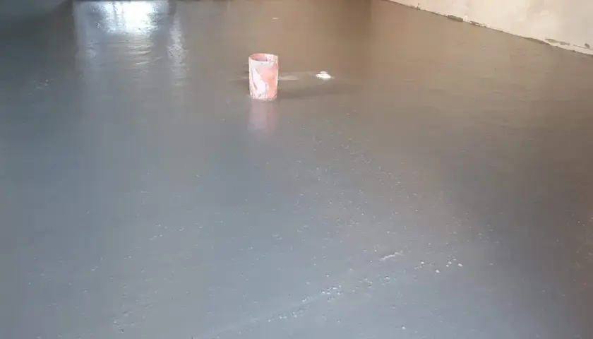 Świeżo wylany, gładki **pianobeton** na podłodze. W tle widać wiaderko i instalacje.