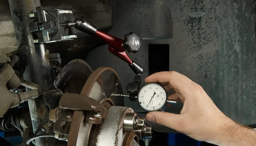 Mechanik sprawdza bicie przy hamowaniu, używając czujnika zegarowego do oceny prostych tarcz hamulcowych.