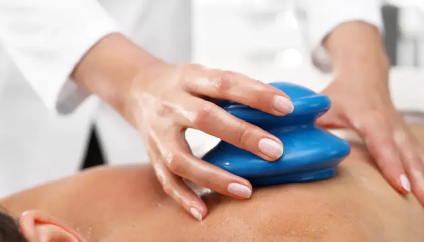 Dłoń terapeuty wykonuje masaż bańką chińską na plecach klienta. Niebieska bańka jest przykładana do skóry, tworząc podciśnienie.