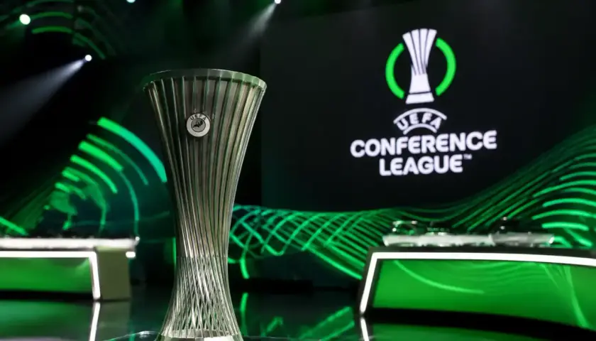 Trofeum Ligi Konferencji UEFA na tle logo i zielonych świateł. Marzenie o wygraniu tych rozgrywek napędza emocje podczas meczów ligi konferencji.