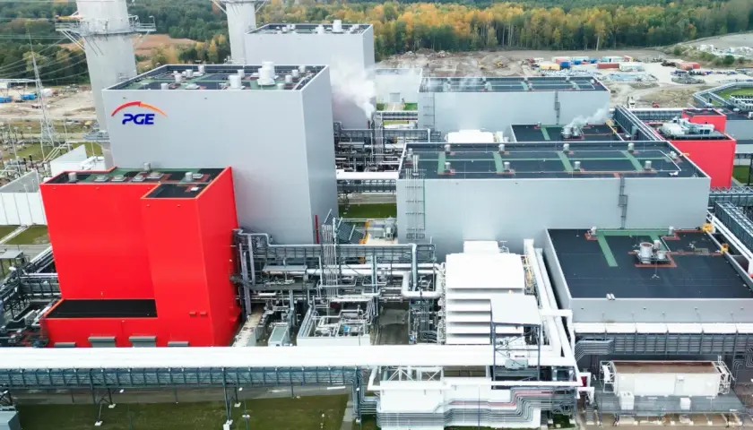 Nowoczesna elektrownia PGE z czerwonym budynkiem i białymi blokami, w tle las i kominy.