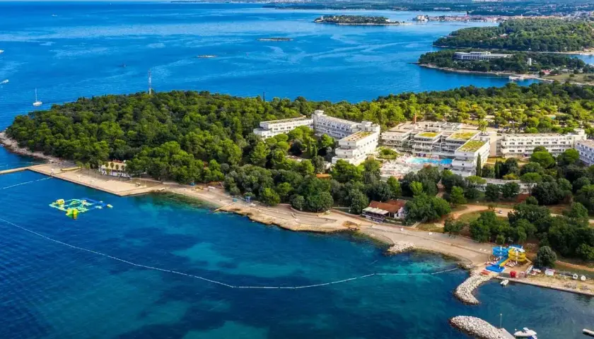 Hotel Delfin Plava Laguna, otoczony zielenią, z basenami i plażą nad turkusowym morzem.