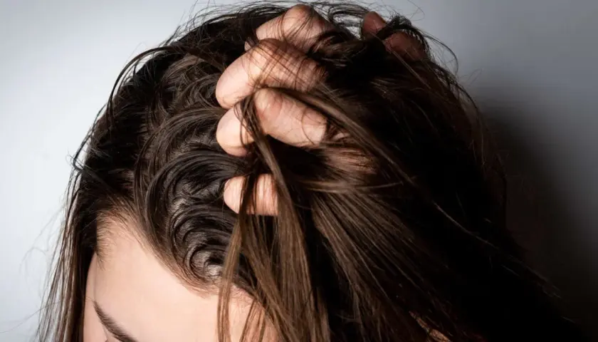 Mano revolviendo cabello oscuro y lacio. ¿Es mejor teñirse con el pelo sucio o limpio?