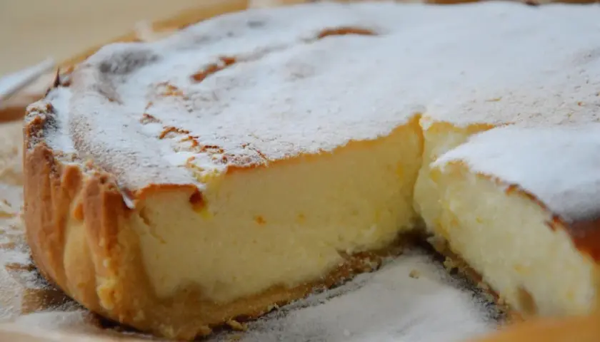 Une part de tarte à la ricotta sucrée, saupoudrée de sucre glace, révèle sa garniture crémeuse et sa croûte dorée. Un délice !