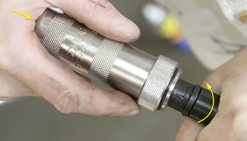 Mani che usano un avvitatore a percussione per svitare una vite spanata. La freccia gialla indica la rotazione.