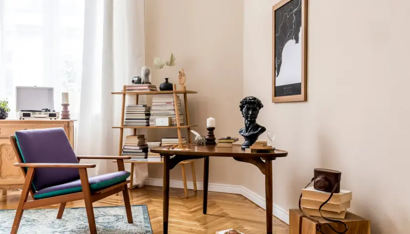 Kącik do czytania w stylu vintage: fioletowy fotel, drewniany stolik z biustem i książkami, regał pełen literatury.