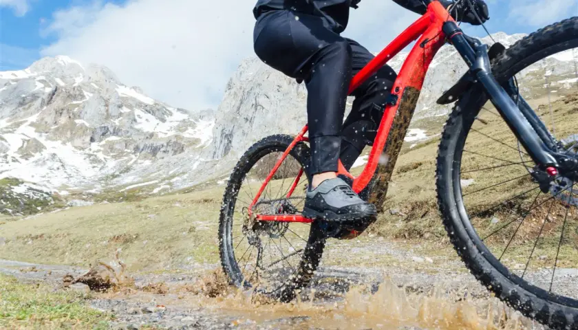Kolarz na czerwonym rowerze trekkingowym pokonuje błotnistą kałużę na górskim szlaku.