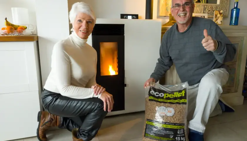 Pareja feliz junto a su nueva estufa de pellets, con una bolsa de combustible lista para la instalación.