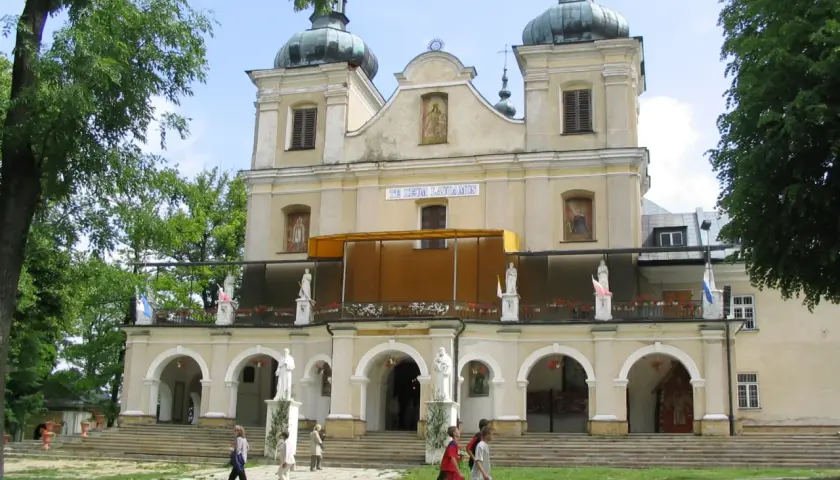 Kalwaria Pacławska: Sanktuarium z kopułami i tarasem, gdzie pielgrzymi spacerują pośród zieleni.