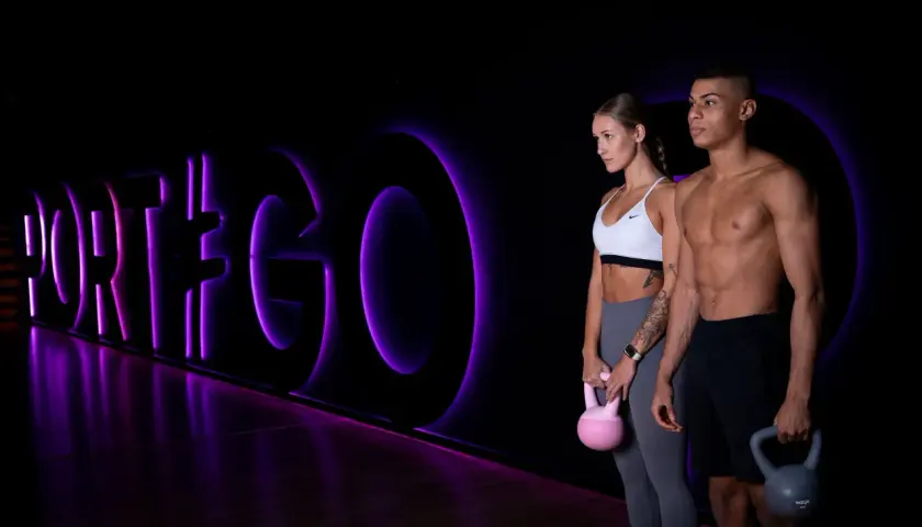Para dwojga z kettlebellami na tle neonowego napisu "PORT#GO".