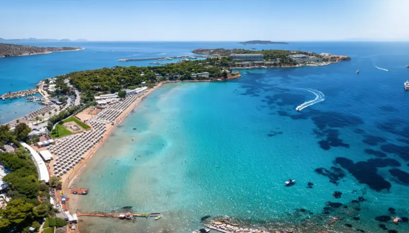 Traumhafter Strand bei Athen mit türkisfarbenem Wasser, Liegestühlen und Booten.