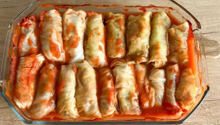 Pyszne, domowe gołąbki w sosie pomidorowym, gotowe do pieczenia. Ile piec gołąbki w piekarniku? Czekają na swój czas w szklanym naczyniu.