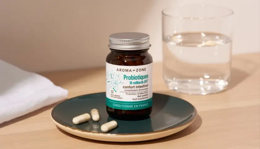 Bouteille de probiotiques Aroma-Zone sur une assiette avec des gélules, à côté d'un verre d'eau. Une cure probiotique pour le confort intestinal.