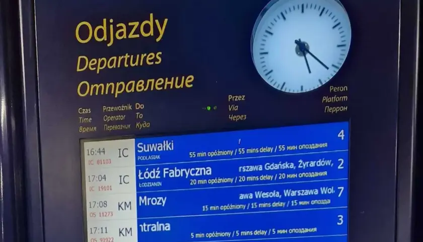 Tablica odjazdów pociągów pokazuje, gdzie sprawdzić opóźnienia pociągu. Widoczne są czasy, kierunki i informacje o opóźnieniach.
