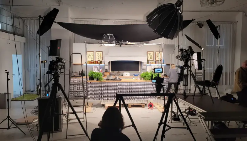 Studio filmowe z kuchnią, kamerami i lampami. Widać tu moc światła, które tworzy atmosferę do nagrania.