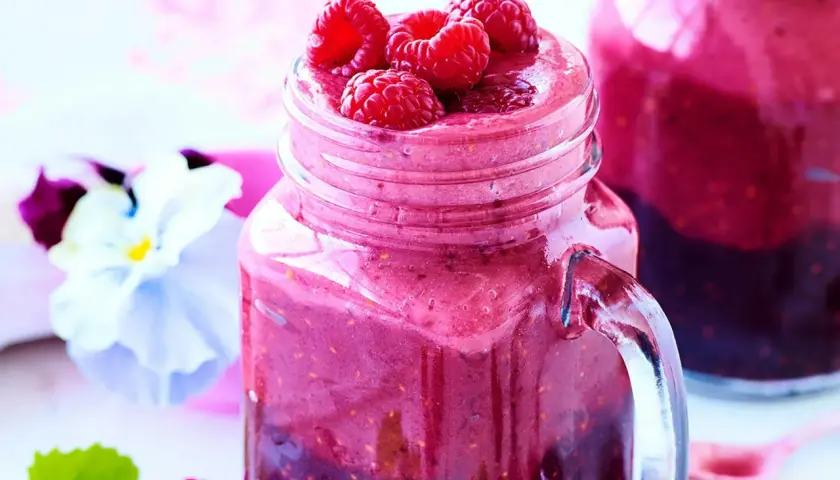 En härlig hallonsmoothie i ett glas med färska hallon på toppen. Ett perfekt smoothie recept för en solig dag.