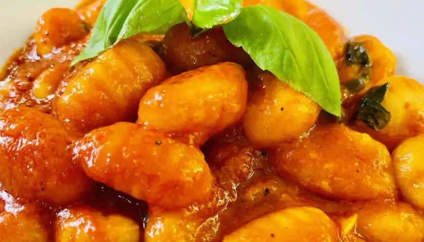 Gnocchi al pomodoro, soffici e avvolti in un sugo rosso brillante, guarniti con foglie di basilico fresco.