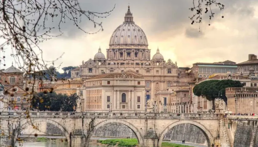 Un ponte di Roma attraversa il Tevere, con la maestosa cupola di San Pietro che domina lo skyline in una giornata invernale.