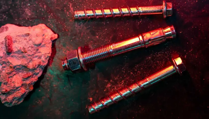 Tasselli e bulloni metallici, con un pezzo di cemento grezzo. La scena è illuminata da luci rosse e verdi, creando un'atmosfera drammatica, ideale per una tabella portata tasselli.