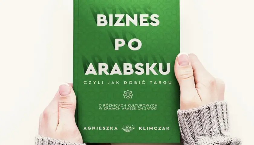 Dwie dłonie trzymają zieloną książkę z białym napisem "Biznes po arabsku".