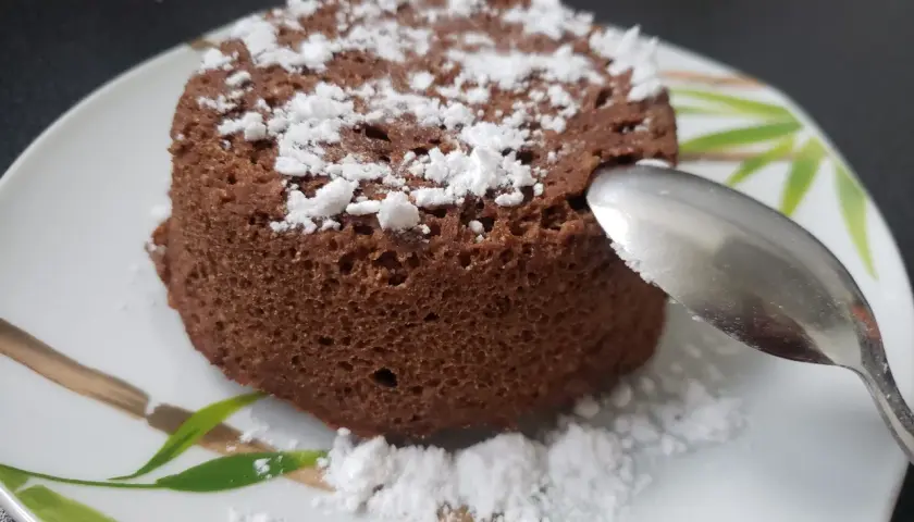 Un délicieux bowl cake au chocolat, saupoudré de sucre glace, prêt à être dégusté avec une cuillère.