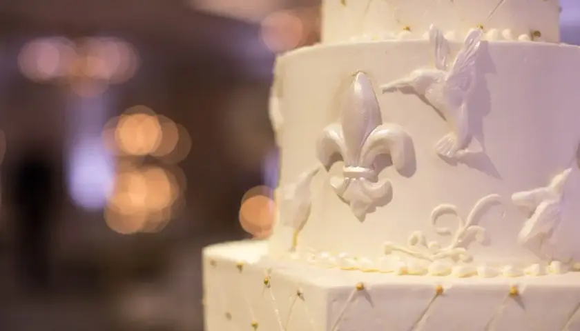 Elegancki tort weselny z ozdobami z masy cukrowej, jak przykleić ozdoby z masy cukrowej do tortu? Delikatne lilie i ptaszki zdobią białe warstwy.