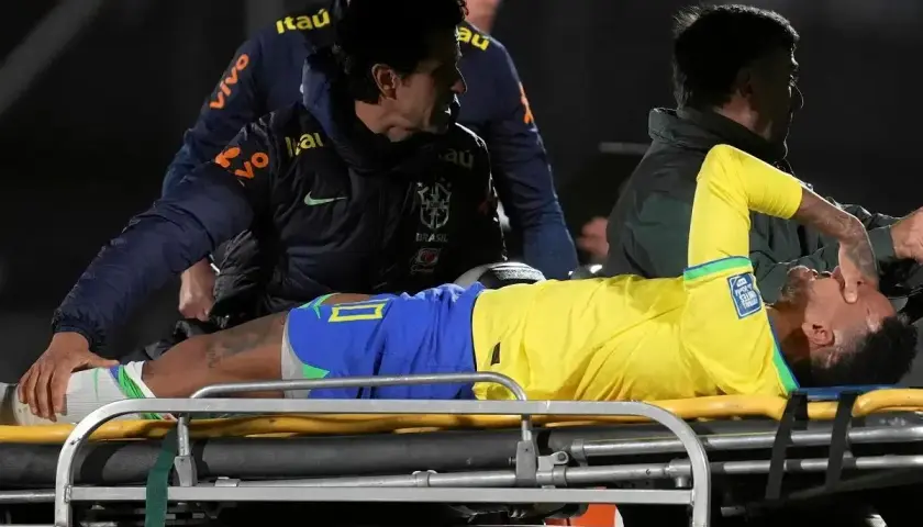 Neymar leży na noszach, z bólu trzymając się za twarz. Jego **neymar kontuzja** wygląda poważnie, a sztab medyczny otacza go troską.