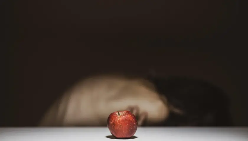 Czerwone jabłko na białym tle, w tle niewyraźna postać.