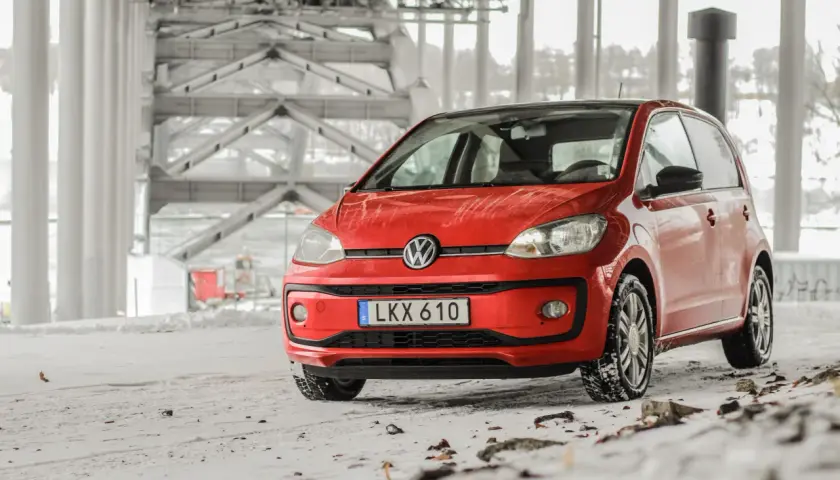 Röd VW Up med vinterdäck står på snöig mark under en bro. Ett vw up problem kan vara att den fastnar i snön.