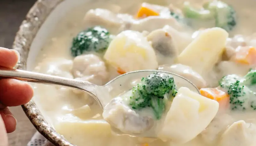 A spoonful of creamy Japanese white stew, filled with tender chicken, potatoes, broccoli, and carrots, ready to be savored.