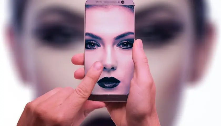 Dłonie trzymają smartfon, na ekranie którego widać twarz kobiety z mocnym makijażem. To przykład zaawansowanej fotografia obliczeniowa.
