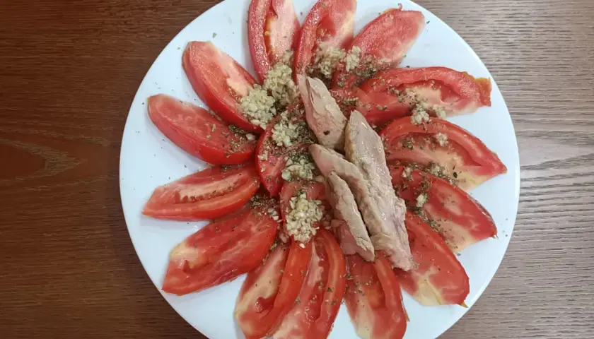 Rodajas de tomate fresco aliñado con ajo picado y hierbas, coronado con trozos de melva. Un plato sencillo y delicioso.