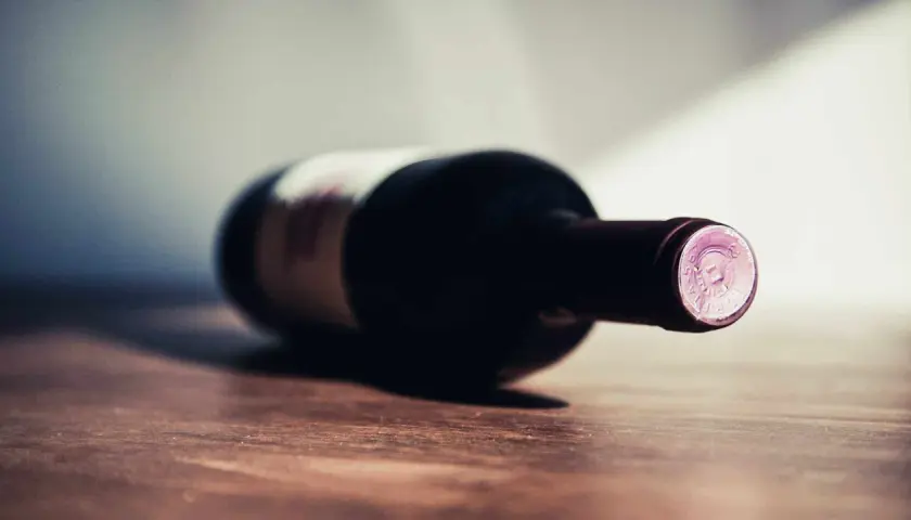 Une bouteille de vin couchée sur une table en bois. La question se pose : 1 bouteille de vin pour combien de personnes ?
