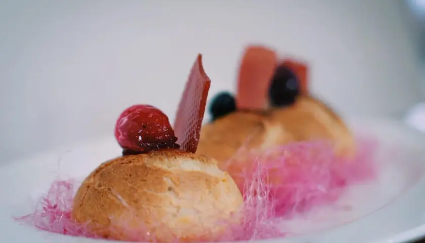 Un ou une profiterole décoré d'une framboise, d'une tuile de chocolat et de barbe à papa rose.