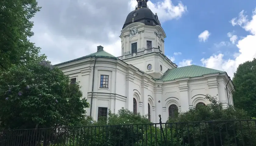 Adolf Fredriks kyrka i Stockholm, en vit kyrka med grön kupol och tak, omgiven av träd och buskar.