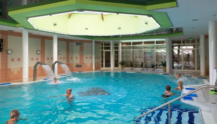 Basen rehabilitacyjny z hydromasażem i wodospadami, w którym kąpią się ludzie.