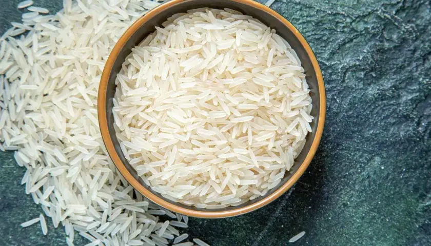Chicchi di riso basmati in una ciotola e sparsi su una superficie scura. Le proprietà del riso basmati lo rendono un alimento leggero e digeribile.