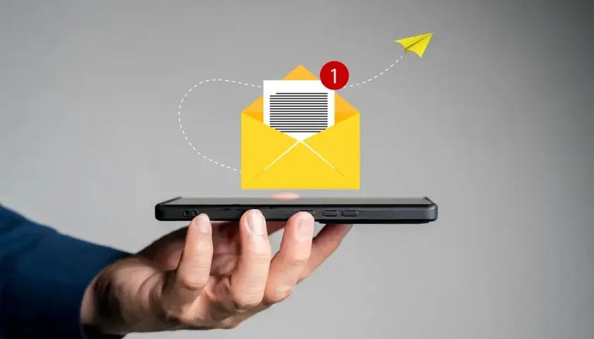 Dłoń trzyma smartfon, z którego wylatuje żółta koperta z powiadomieniem. Pomysł na to, co napisać w SMSie o urlop na żądanie.
