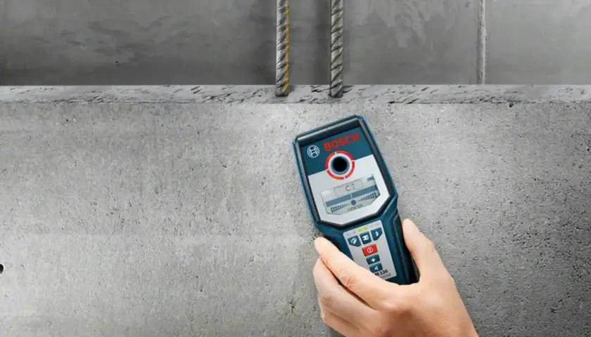 Hand håller en Bosch-detektor för att undvika att borra i armeringsjärn i betongvägg.