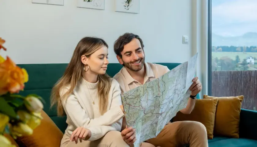 Para planuje podróż, przeglądając mapę. W tle widać krajobraz z domkami, przypominający widok z **Osolina**.