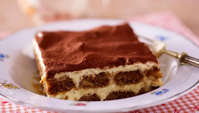 Ein Stück Tiramisu, ein Klassiker der italienischen Nachspeisen, auf einem Teller mit Kakaopulver bestäubt.