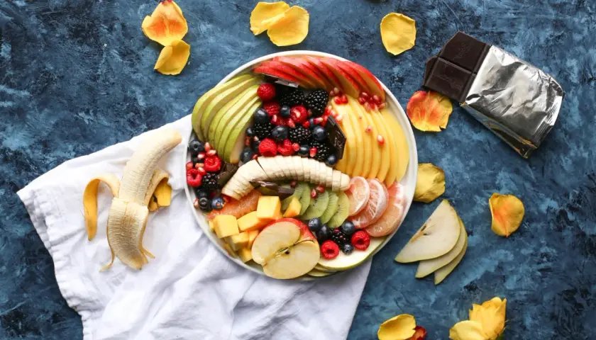 Plato de frutas variadas, incluyendo plátano, manzana, kiwi, bayas y cítricos. Es bueno comer fruta por la noche.