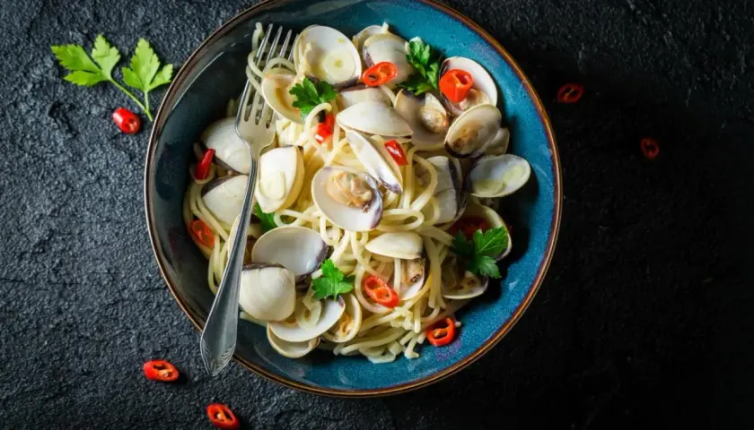 Makaron spaghetti z aromatycznymi vongole, czosnkiem i ostrą papryczką, udekorowany natką pietruszki.