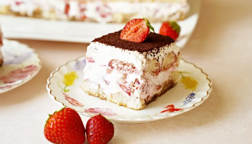 Pyszne tiramisu truskawkowe z bitą śmietaną, biszkoptami i świeżymi truskawkami, posypane kakao.