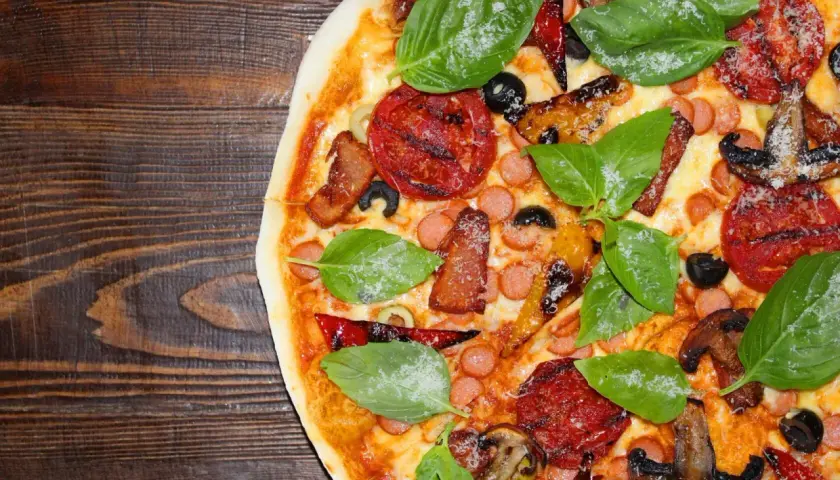 Pyszna california pizza z kiełbaskami, bekonem, pieczarkami i świeżą bazylią na drewnianym blacie.