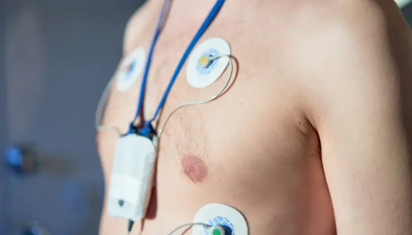Mężczyzna z elektrodami EKG na klatce piersiowej, podłączony do urządzenia monitorującego. To właśnie holter, co to jest? Badanie serca.