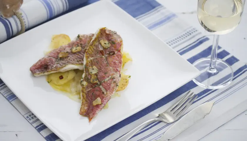 Dos deliciosos salmonetes al horno, con láminas de ajo y perejil, servidos sobre patatas. Un plato perfecto para disfrutar.
