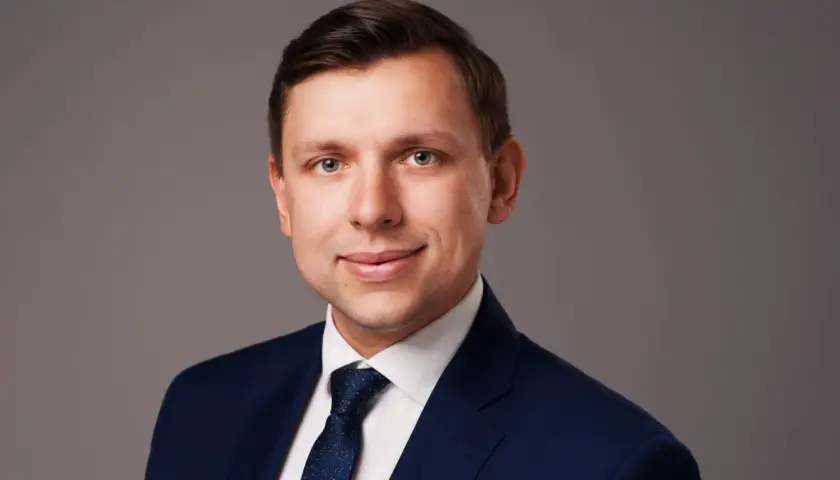 Portret mężczyzny w granatowym garniturze i białej koszuli z krawatem.